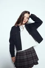 Campera de jean color negro con cuello de pana en tono marrón, cierre frontal con botones y bolsillos en el pecho. Presenta un diseño de corte relajado y ligeramente cropped, con interior forrado en corderito para mayor abrigo.