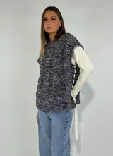 Chaleco de punto grueso color azul y beige, con cuello redondo y sisas. Presenta un detalle de cordones blancos entrelazados en los laterales.