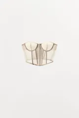 Corsé strapless color beige claro, con copas con aros y estructura de varillas verticales. El tejido es semitransparente con pequeños lunares visibles. Presenta un cierre frontal con ganchos.