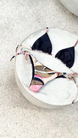 Bikini reversible de diseño triangular con tiras para atar y apliques de argollas metálicas. El conjunto presenta un estampado abstracto multicolor.