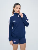 Buzo de felpa azul marino con medio cierre, cuello alto, bandas laterales en tono rosado y bolsillo frontal tipo canguro. Presenta el logo de Umbro y el escudo del Club Nacional de Football bordados.