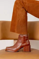 Bota corta de cuero color marrón, con taco cuadrado texturizado y punta cuadrada. Presenta un diseño minimalista con cierre lateral y tirador en la parte trasera.