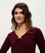Blusa de pijama de manga larga color bordó, confeccionada en viscolycra. Presenta escote en V con ribete de encaje en tono contraste, frunce frontal y un delicado lazo decorativo.