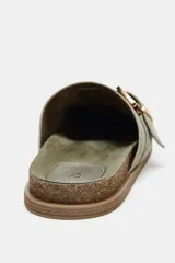 Zueco plano de serraje color verde oliva, con punta redonda y detalle de tira con hebilla metálica dorada en el empeine. Cuenta con plantilla de efecto aterciopelado y suela de corcho.