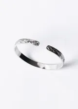 Pulsera esclava abierta de acero quirúrgico plateado con diseño esculpido en los extremos.