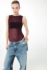 Body sin mangas de cuello redondo, confeccionado en una combinación de tul transparente y paneles de tela opaca a tono. Presenta un diseño ajustado con cierre inferior mediante botones a presión.
