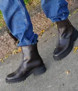 Botas de cuero color marrón chocolate con suela de goma tipo track en color negro. Presentan un diseño de caña media con cierre frontal metálico y costuras reforzadas.