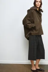 Trench corto de corte recto con capucha y cuello desmontable efecto pelo. Presenta cierre frontal con botones, bolsillos laterales y mangas largas con trabillas en los puños.