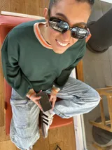 Buzo verde oscuro de algodón, con cuello redondo y puños acanalados con borde naranja.