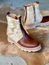 Botas de cuero marrón con paneles laterales de corderito en color crema. Presentan una suela track de goma en color beige, cierre lateral interno para facilitar el calce y tirador en la parte posterior.