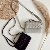 Cartera bandolera negra de ecocuero con diseño acolchado en rombos. Tiene asa corta superior y correa larga desmontable y regulable.