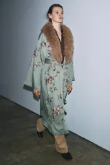 Kimono de largo midi en color verde grisáceo, con cuello de solapas amplias en pelo sintético marrón. Presenta mangas largas acampanadas y un cinturón ajustable del mismo tejido. El diseño está decorado con un delicado bordado floral en tonos tierra y rosados.