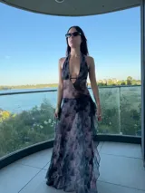 Vestido largo de color chocolate, con escote halter profundo y diseño de falda con volados laterales. Presenta una silueta fluida y transparente.