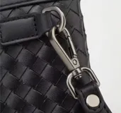 Sobre o clutch negro de eco cuero con diseño tejido en patrón de rombos. Incluye una correa de muñeca desmontable.