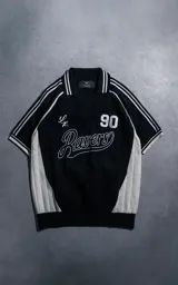 Chomba deportiva de tejido de punto con cuello polo y cierre frontal en V. Presenta diseño bicolor en negro y blanco, con detalles de rayas en hombros y mangas, y estampado frontal con el texto 'Ravers' y el número '90'.