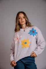 Buzo negro de tejido texturizado con apliques de flores de crochet en colores rosa pálido, amarillo y azul. Tiene cuello redondo y mangas largas.