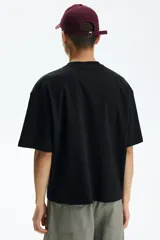 Remera negra de corte oversized y silueta holgada, confeccionada en punto liviano de algodón, con cuello redondo ribeteado y mangas cortas de hombros caídos.
