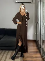 Vestido largo color marrón, con escote en V, mangas largas con puños y detalle de encaje en el pecho. Presenta un diseño asimétrico con volados en el ruedo y una abertura frontal.