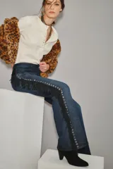 Jean de corte recto y tiro medio, color azul oscuro, con detalle de flecos negros y ojales metálicos a lo largo de la costura lateral.