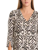 Blusa de seda fría con estampado geométrico tipo ikat en tonos beige y negro. Presenta escote en V, botones decorativos en la parte frontal y mangas tres cuartos con detalle de tajo en los puños.