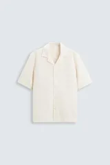 Camisa de manga corta color crema, con cuello bowling y tejido texturizado. Corte regular fit con aberturas laterales en el bajo.
