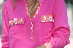 Camisa fucsia de viscosa con detalles pintados a mano en cobre, rosa y blanco en cuello, bolsillos y puños. Presenta mangas largas, cuello en V con escote abotonado y bolsillos frontales con solapa.