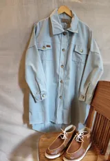 Chaqueta de acrocel color celeste, de manga caída y largo medio, con bolsillos frontales con solapa, cierre de botones y terminación desflecada.