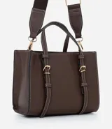 Bolsa tipo satchel de tamaño mediano, color marrón, con diseño estructurado y costuras decorativas en contraste. Presenta dos correas de mano fijas con detalles de hebillas metálicas doradas y una correa larga desmontable de tela. Cuenta con cierre superior por cremallera.