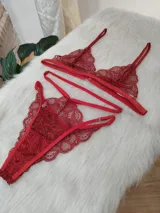 Conjunto de lencería de encaje color rojo, compuesto por un bralette triangular con breteles finos y una tanga con diseño de tiras cruzadas y detalles de encaje.