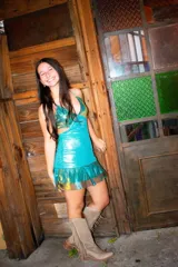 Vestido corto de tela metalizada en tonos turquesa y dorado, con escote en V, diseño de top triangular, aberturas laterales en la cintura y doble volado irregular en el ruedo.