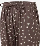 Pantalón de pijama tipo jogger, color marrón con estampado floral pequeño en blanco. Presenta cintura elástica con lazo de ajuste frontal y puños ajustados en los tobillos.