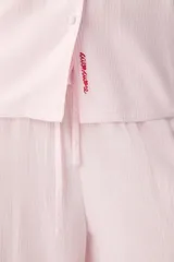 Pijama rosado de 100% viscosa con diseño a rayas sutiles, compuesto por una camisa de manga larga con cuello solapa y botones delanteros, y un pantalón largo de corte holgado con cintura elástica y cordón ajustable. Presenta un pequeño detalle bordado de corazón rojo en el pecho de la camisa.