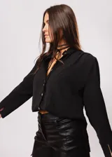 Camisa negra de cuello redondo con frunces y mangas largas con puños abiertos.