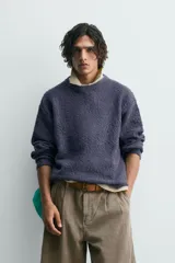 Jersey de hombre de corte relajado, color azul oscuro o morado apagado, con textura rizada (bouclé) y cuello redondo.