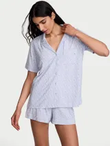 Pijama corto de Victoria's Secret confeccionado en suave mezcla de modal, de color celeste con estampado de monogramas. Incluye una camisa de manga corta con solapas, cierre frontal de botones y un bolsillo en el pecho, acompañada de un short con cintura elástica.