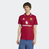 Camiseta de fútbol Adidas del Manchester United, modelo Home 26/27. Diseño en color rojo con cuello polo y puños a rayas en blanco y negro, con detalles de las tres tiras de Adidas en los hombros y el logo de Snapdragon en el frente.