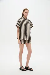 Camisa de algodón de corte holgado, con diseño de rayas verticales en colores negro y beige, cuello camisero y cierre frontal con botones.