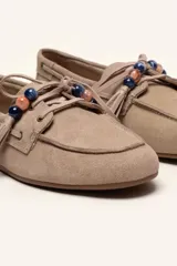 Mocasín estilo náutico de gamuza marrón, con cordones de cuero, borla decorativa y cuentas de colores en el empeine.