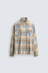 Camisa de manga larga con cuello solapa y dos bolsillos frontales de plastrón con botón. Presenta un estampado de cuadros en tonos beige, azul claro y marrón.