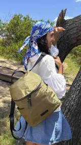 Mochila urbana de diseño compacto en color verde oliva, con cierre principal de doble cursor, bolsillo frontal con cierre y correas ajustables negras. Presenta un estilo minimalista y funcional.