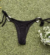 Conjunto de bikini negro con corpiño triangular con argolla metálica y bombacha colaless con tiras para atar y argollas en los costados.