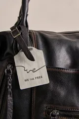 Bolso tote de cuero lavado negro con efecto gastado, interior amplio, bolsillos exteriores con cremallera, dos asas de mano y correa desmontable y regulable.