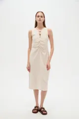 Vestido midi de viscosa color beige, sin mangas y con cuello a la base. Presenta una abertura frontal con botones decorativos y detalles de frunces en el centro del pecho.