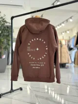 Canguro oversize marrón con capucha, bolsillo tipo canguro y diseño estampado en la espalda con el texto "Be Brave" y detalles tipográficos en color blanco.