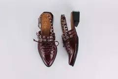 Sueco de cuero color borgoña con cordones, ojales y hebillas plateadas. Tiene tira trasera regulable con elástico.