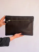 Funda para laptop de cuero natural color negro, con cierre superior y bolsillo frontal con cierre metálico.