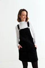 Jumper corto de pana negra con tirantes ajustables, bolsillos frontales y corte recto.