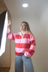 Sweater estilo rugby a rayas horizontales rosas y rojas con cuello blanco y cierre parcial con botones.