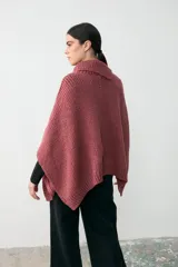 Capita de tejido de punto grueso en color rosa, con cuello alto y diseño holgado tipo poncho con aberturas laterales para los brazos.