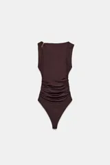 Body negro de manga corta con escote asimétrico, detalle de fornitura metálica dorada en relieve en el hombro y tejido drapeado en el torso. Cierre inferior con botones a presión.